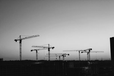 Silhouette cranes against clear sky