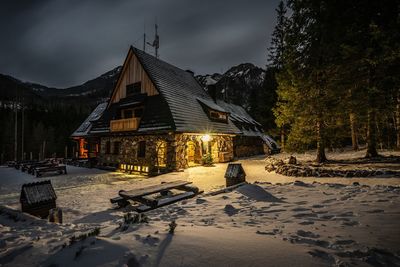 Snow covered houses by building against sky at dusk