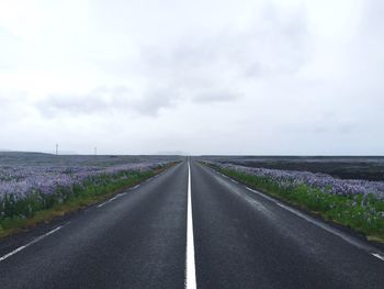 Empty road amidst field against cloudy sky