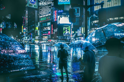 Rear view of people walking on illuminated street at night