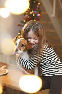 Smiling girl embracing while sitting at home during christmas