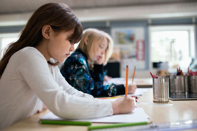 Side view of students writing on paper at desk in classroom