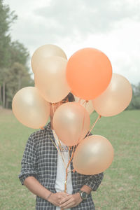 Low angle view of person holding balloons against sky