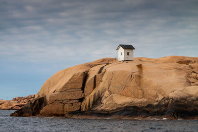 Hut on rock formation at sea shore against sky