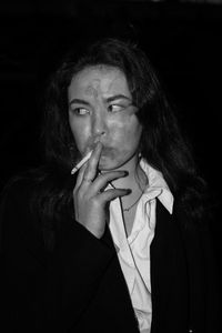 Portrait of young woman smoking cigarette against black background