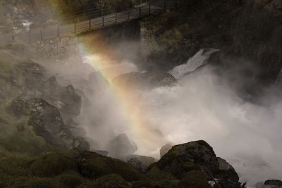 Waterfall crossing under a bridge and the rainbow in a rocky mountain 