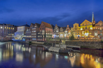 Illuminated buildings by river against sky at dusk