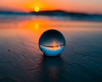 Close-up of crystal ball on beach against sky during sunset