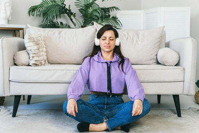 A woman in headphones listens to meditation at home on the floor.