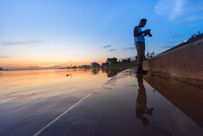 Silhouette man on shore against sky during sunset