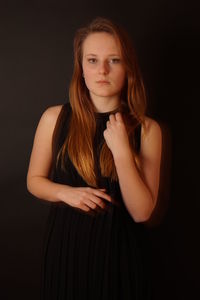 Portrait of beautiful young woman standing against black background