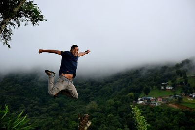 Man jumping in mid-air against mountains during foggy weather