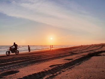 People walking at beach against sky during sunset