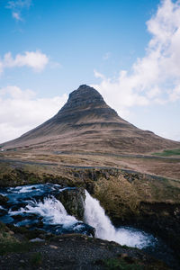 Scenic view of waterfall by kirkjufell against cloudy sky