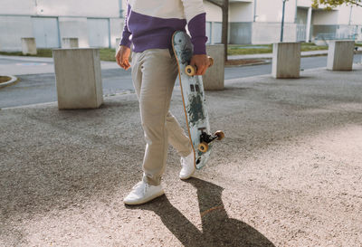 Low section of man carrying skateboard on street