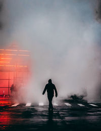 Silhouette man walking on street against smoke in city