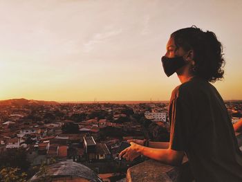 Young woman looking at city buildings against sky during sunset