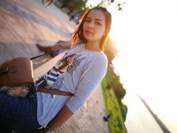 Portrait of young woman with shoulder bag standing at beach against clear sky on sunny day