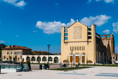 Low angle view of buildings in front of walkway against cloudy blue sky on sunny day