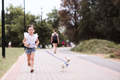 Funny baby girl 3-4 year old run with pet dog in park. looking at camera. childhood. togetherness