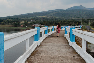 Woman walking on footbridge over lake against mountains