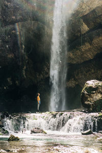 A tiny figure of a young active female tourist at a large mountain waterfall.