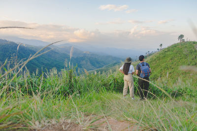 Rear view of people walking on field against sky during sunset