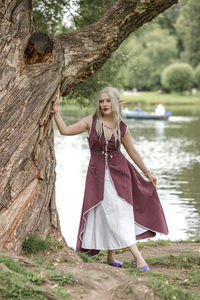 Portrait of young woman standing against tree trunk