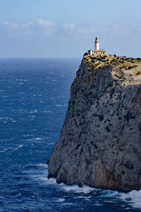 Lighthouse on rocks by sea against sky