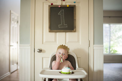 Baby boy eating cake while sitting on high chair at home during birthday