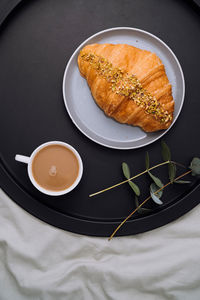 Flat lay of cup of cappuccino, croissant and eucalyptus branch on the tray on bed	
