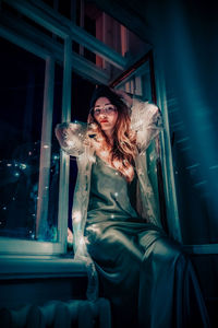 Portrait of woman with illuminated string light sitting on window sill