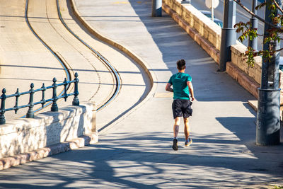 Rear view of man walking on footpath during sunny day