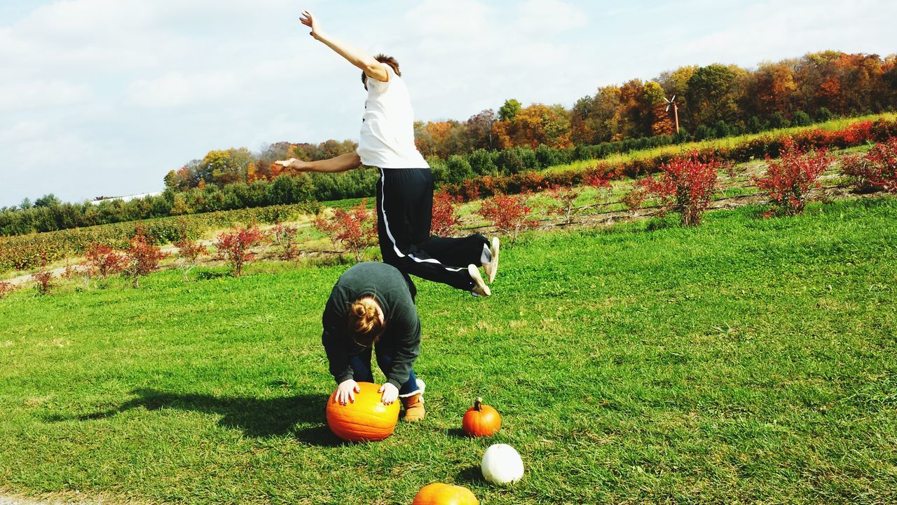 lifestyles, leisure activity, mid-air, full length, jumping, grass, arms outstretched, fun, person, enjoyment, arms raised, casual clothing, freedom, young adult, sport, balance, carefree, tree