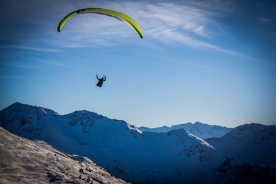 Person paragliding over mountains against sky