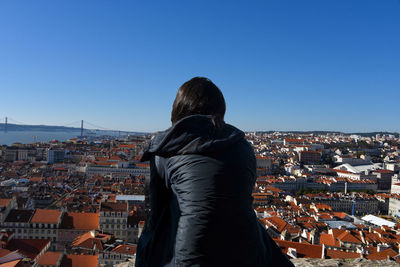 Rear view of woman standing by town against blue sky
