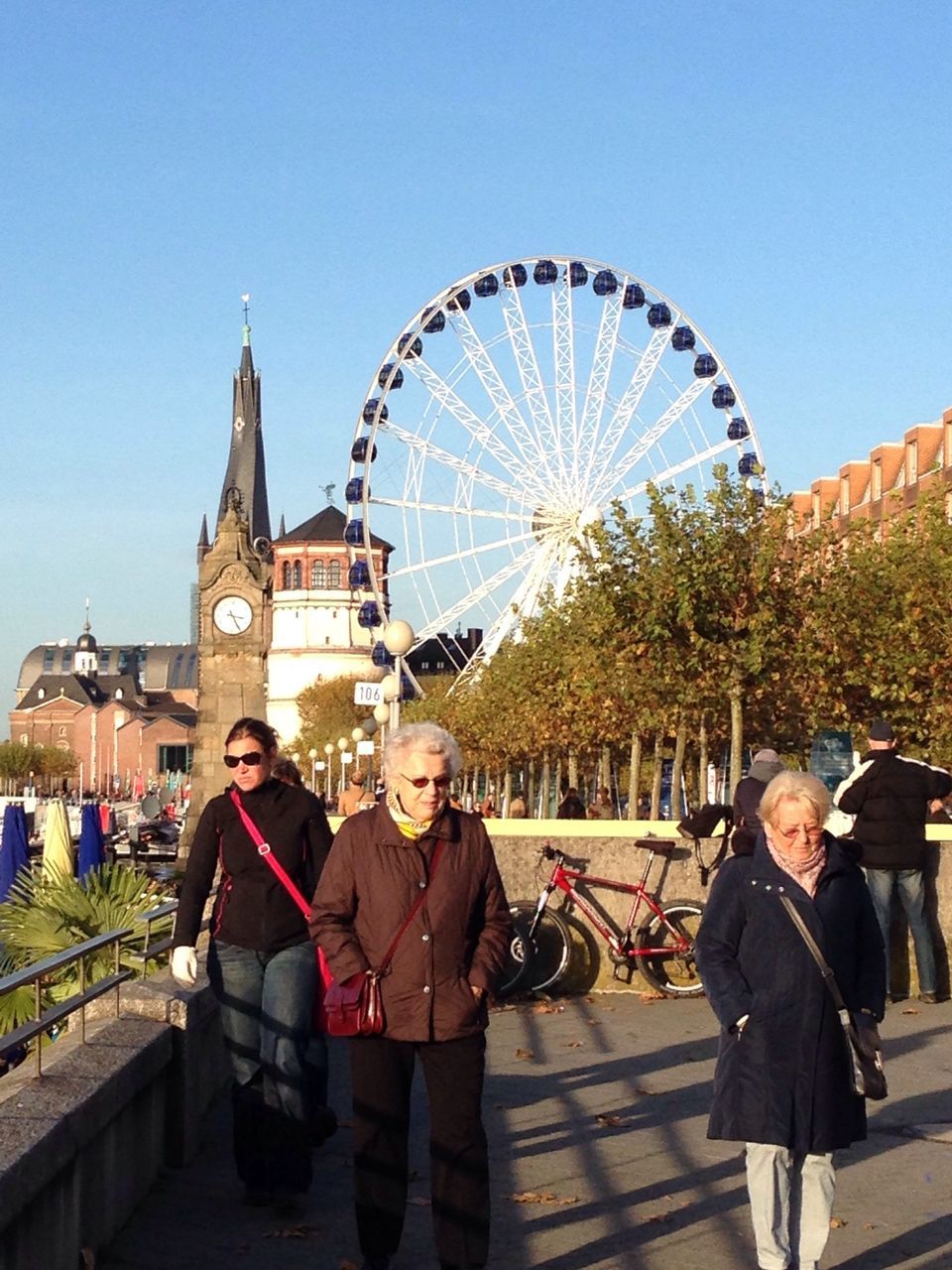 lifestyles, leisure activity, men, person, amusement park, arts culture and entertainment, amusement park ride, architecture, built structure, clear sky, large group of people, ferris wheel, tourism, casual clothing, tourist, standing, travel, building exterior, sky