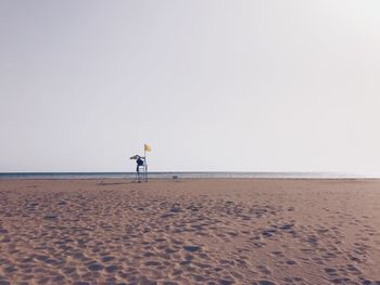 Man sitting alone on beach in watchtower against clear sky