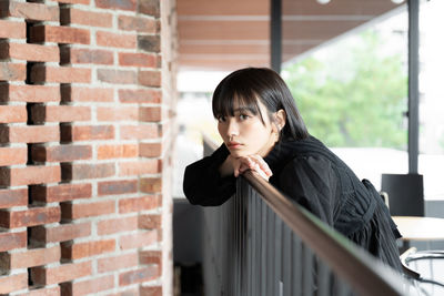 Young woman looking away against brick wall