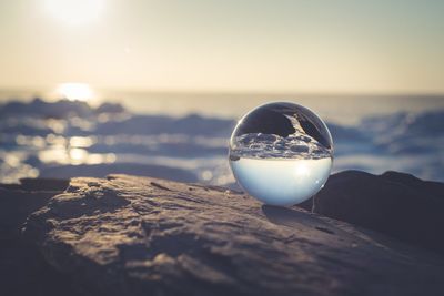 Close-up of crystal ball on rock at sea shore against sky