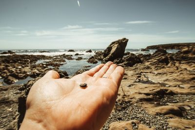 Midsection of person on rock at beach against sky