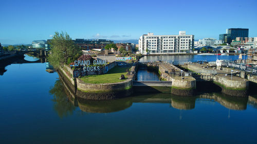 Bridge over river by buildings against clear blue sky