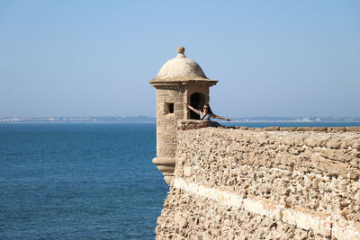 Lighthouse by sea against clear sky