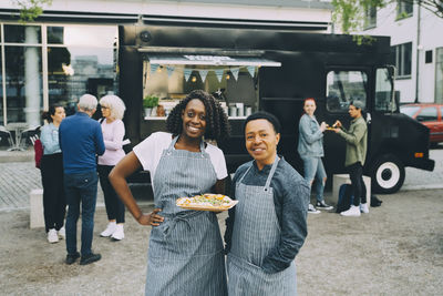 Portrait of smiling owners with indian food plate standing in city