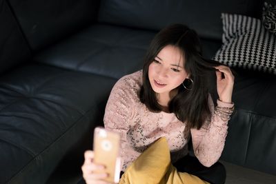 Young woman using phone while standing on sofa