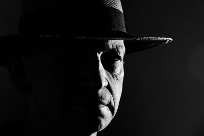Close-up of man wearing hat against black background