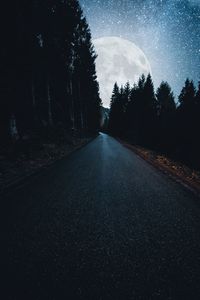 Road amidst trees against sky at night