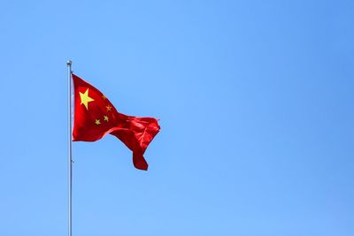 Low angle view of chinese flag against clear blue sky