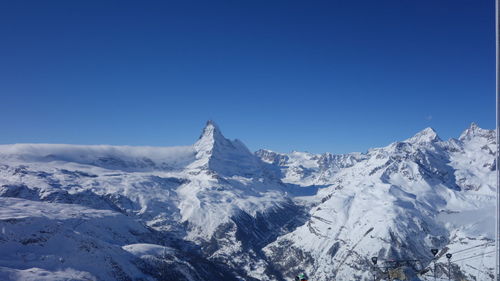 Low angle view of snowcapped mountains against clear blue sky