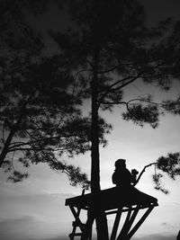 Silhouette man sitting on bench by tree against sky